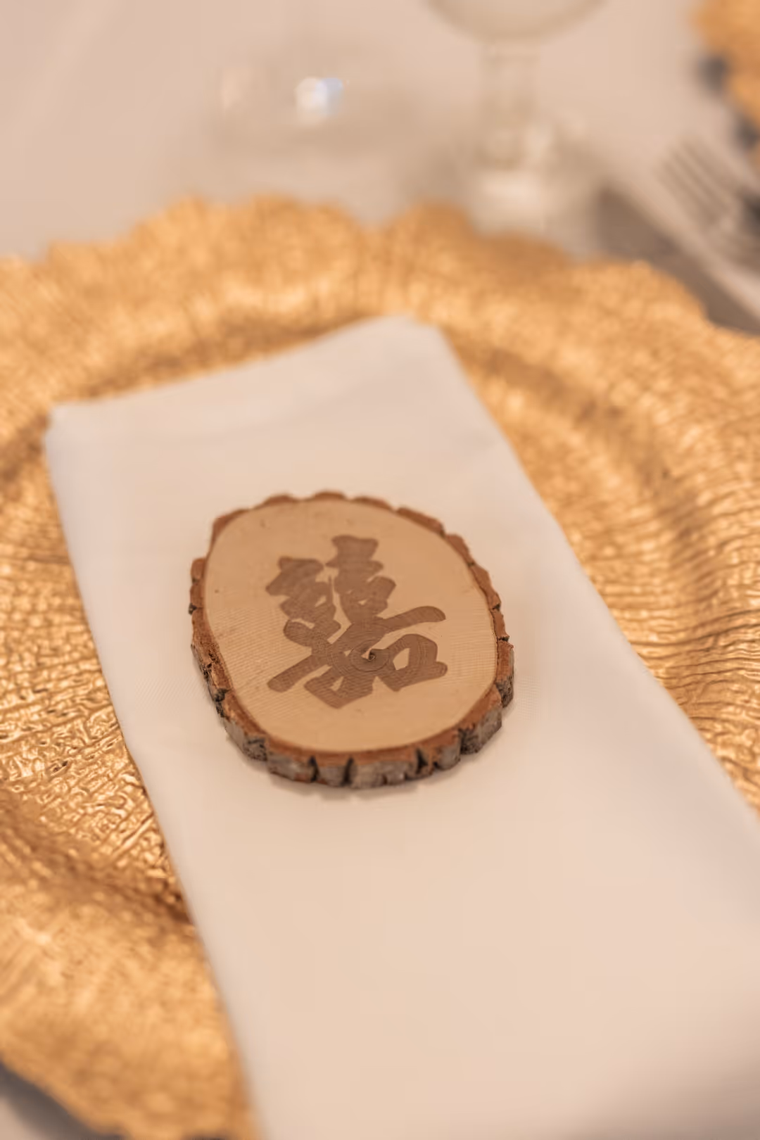 Wood slice with Chinese character on folded white napkin atop textured gold plate.