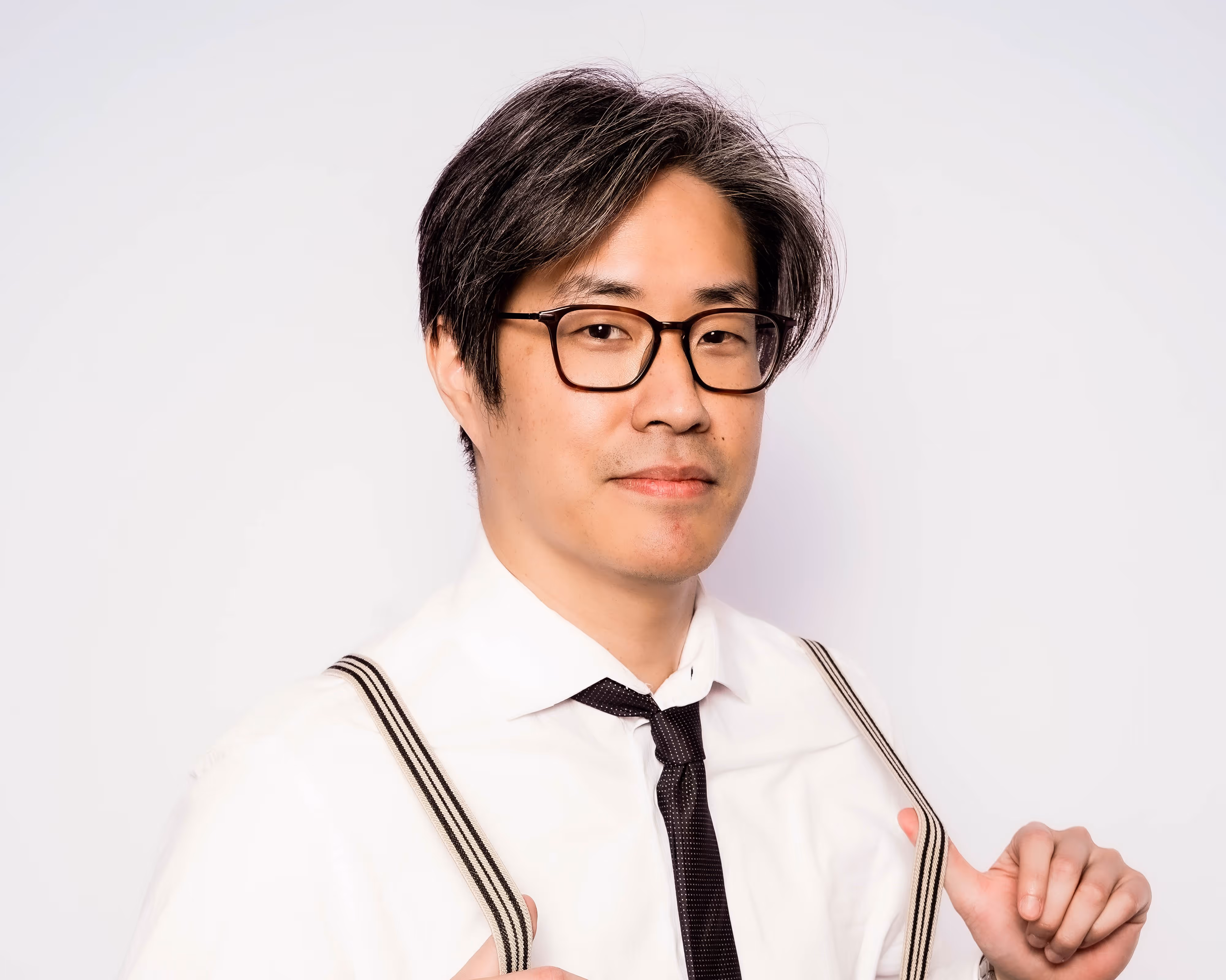 Man with glasses wearing a white shirt, black tie, and striped suspenders against a white background.
