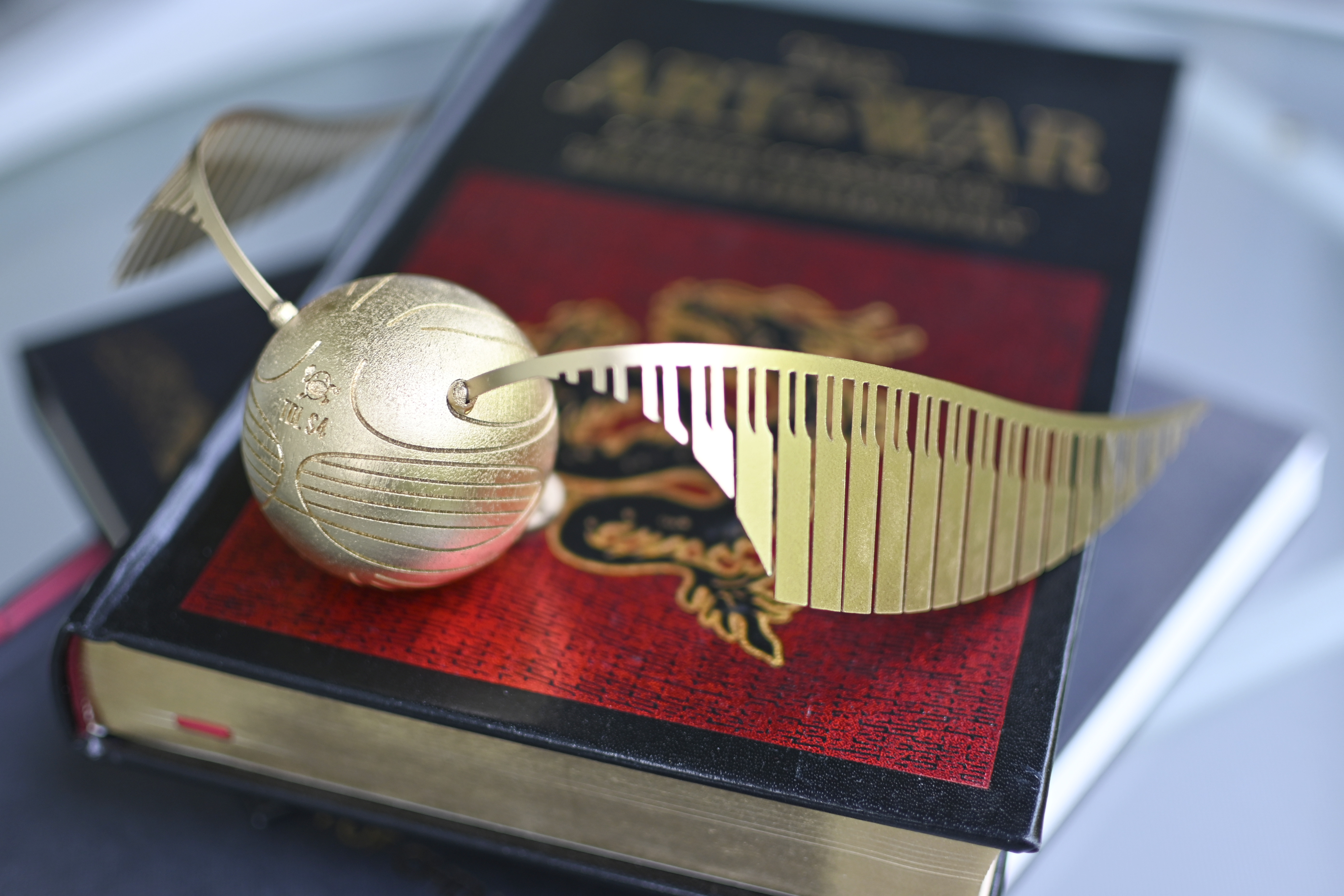 Golden snitch model with wings resting on a red and black Harry Potter book.