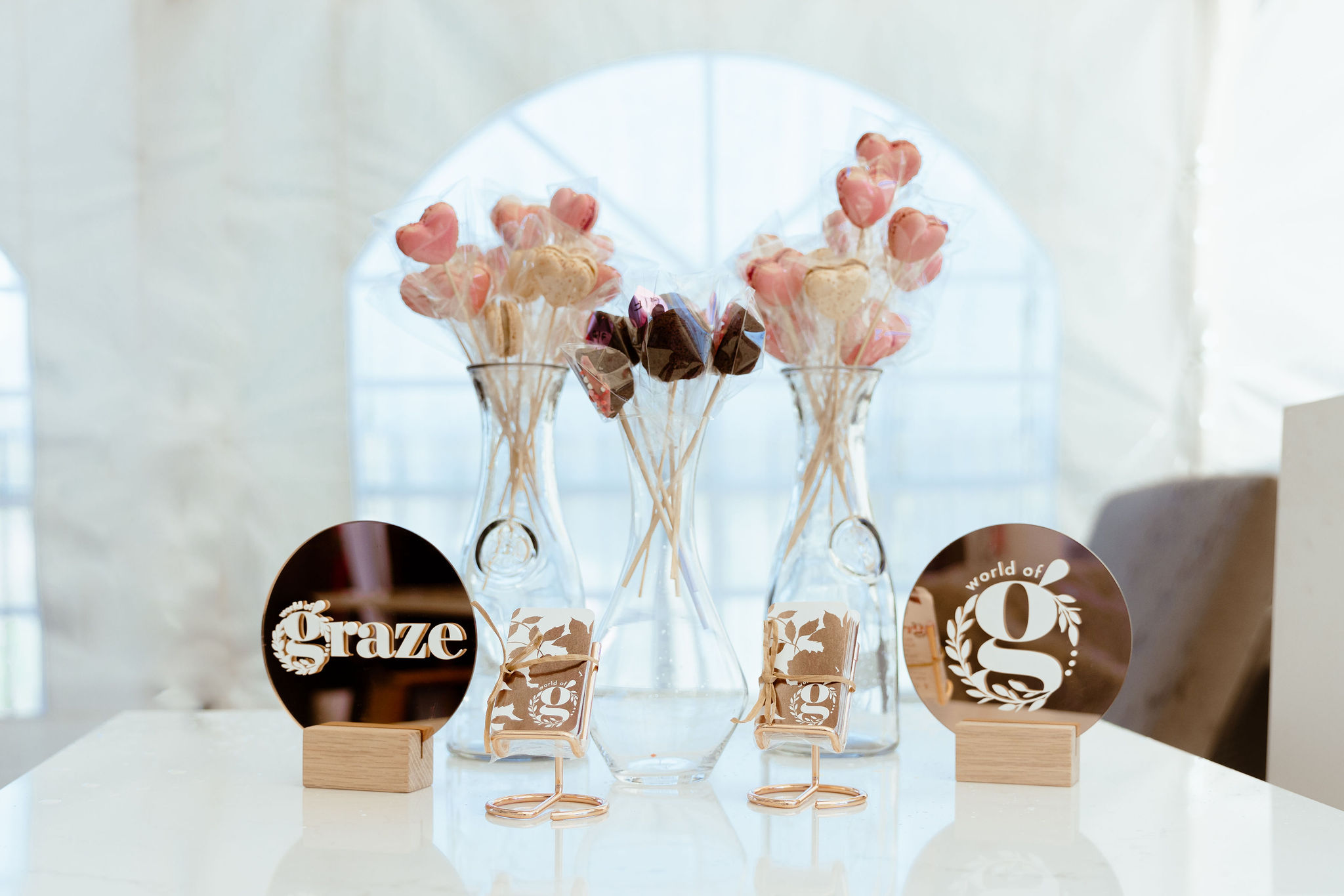 Glass vases with heart-shaped lollipops and two round mirrored signs with Graze and world of g logos.