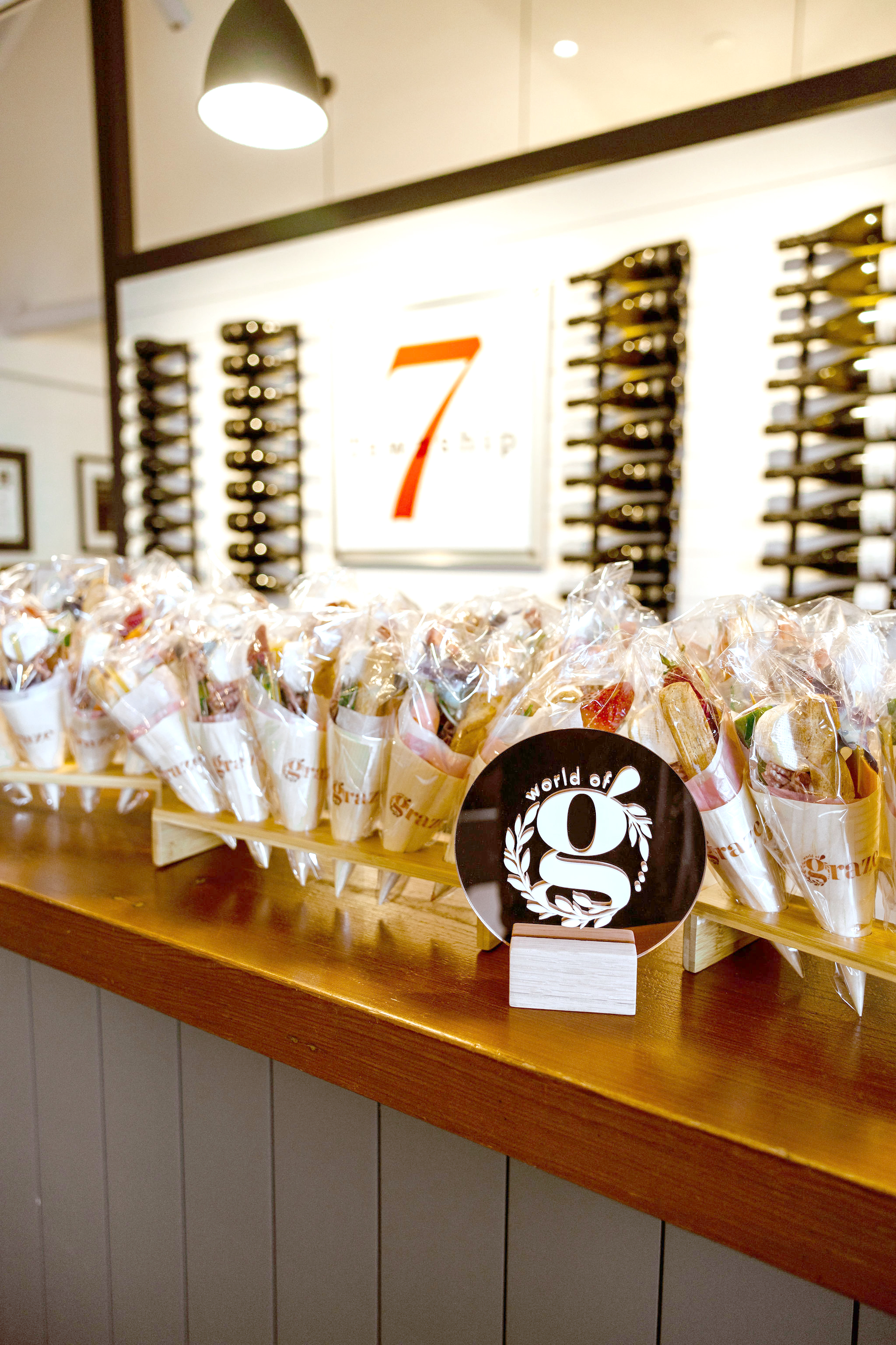 Table with rows of wrapped sandwich cones and a 'world of g' sign on a wooden stand.
