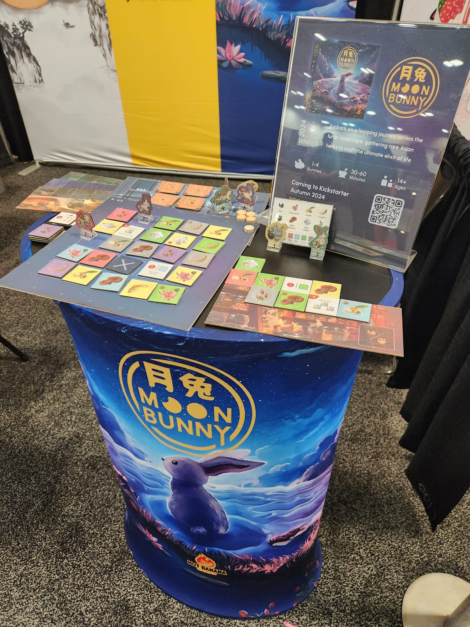 Display of laser-cut Moon Bunny board game with game pieces, cards, and promotional sign on a round table.