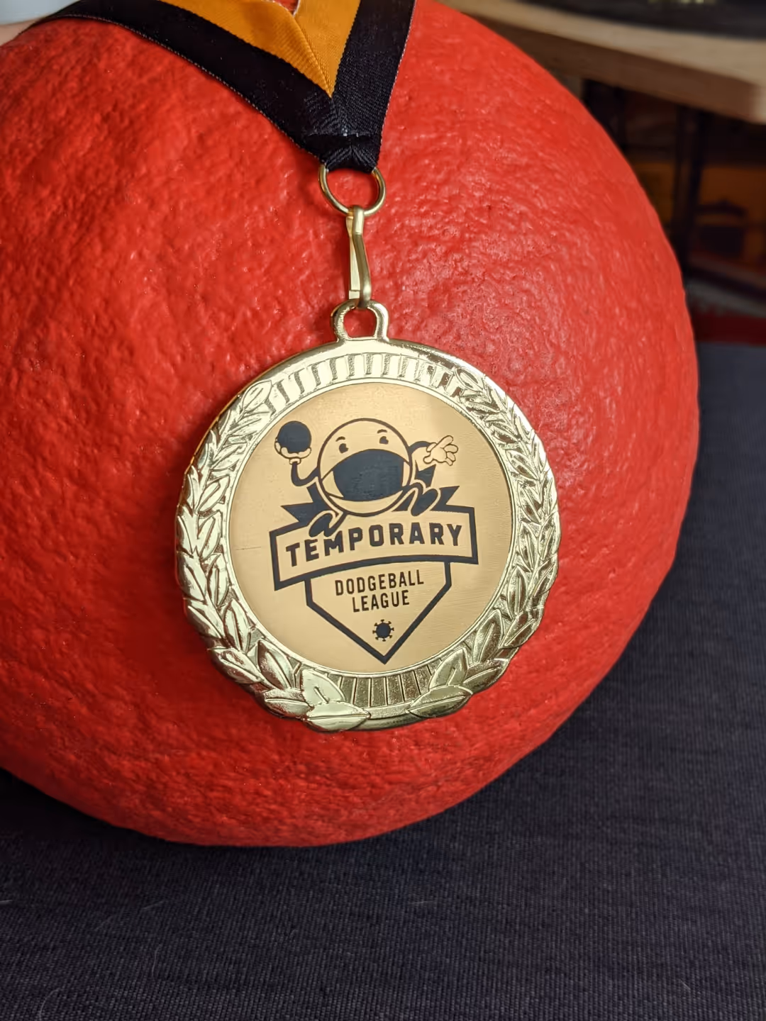 Gold medal with Temporary Dodgeball League logo hangs on a red dodgeball.