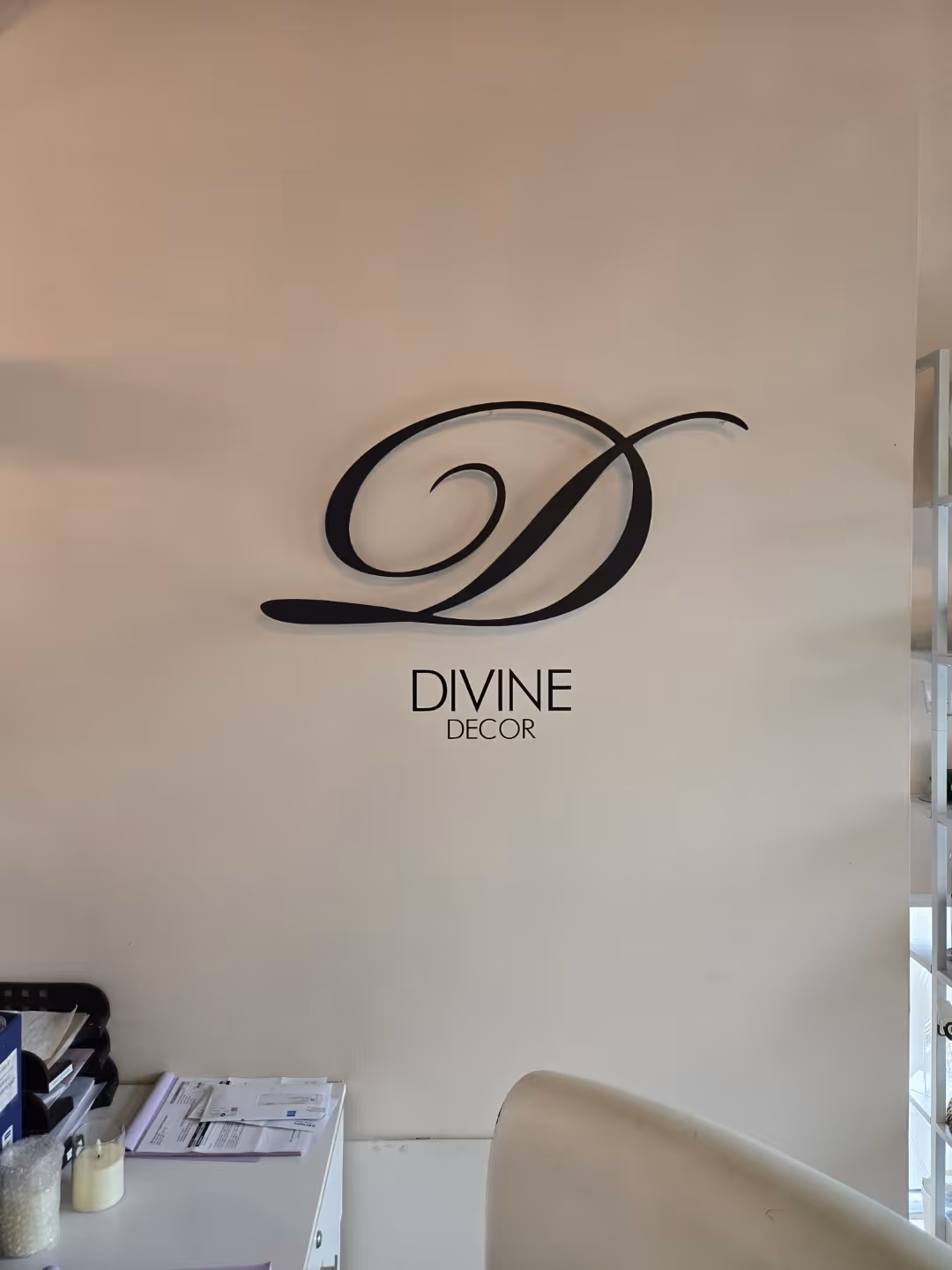 Wall art logo with large script D above the words Divine Decor on a pale beige wall.