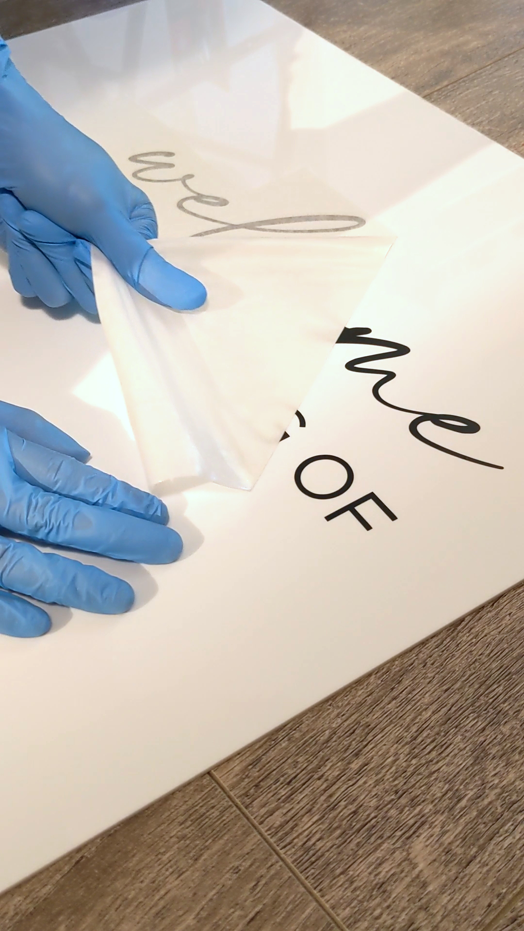 Gloved hands peeling the protective film off a freshly cut acrylic wedding sign with script text.