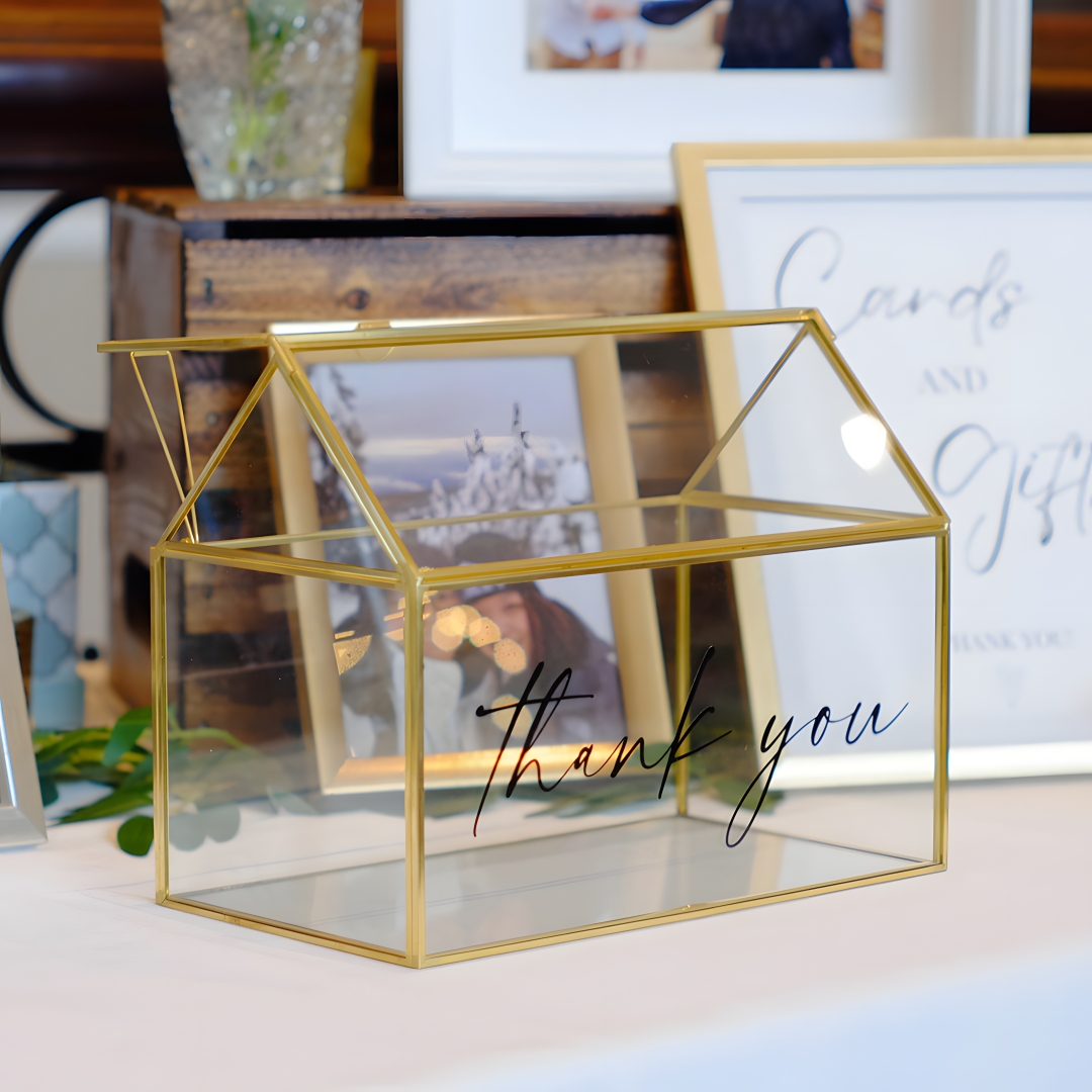 Glass geometric card box with a "thank you" vinyl decal, displayed on a gift table alongside a "Cards and Gifts" sign and framed wedding photos.