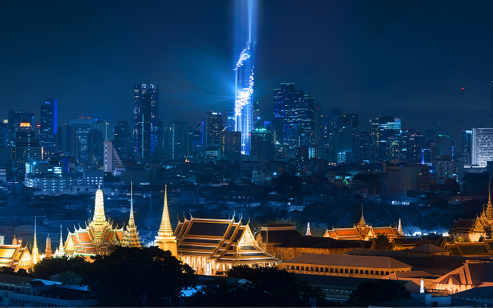 Lit temples in foreground with city skyscrapers and a bright vertical light beam at night.
