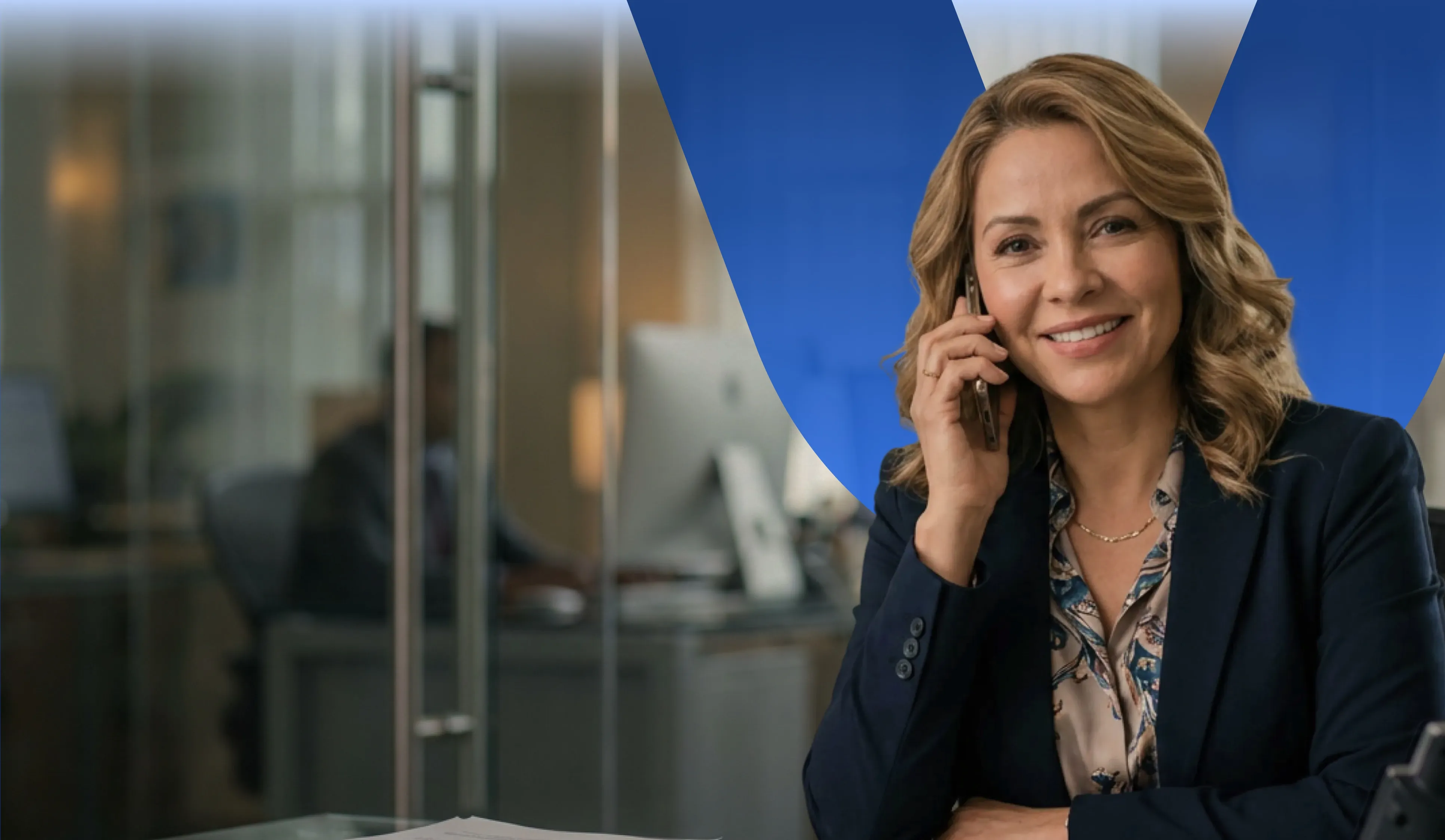Mujer sonriente usando un teléfono móvil en la oficina con fondo de escritorio y computadora.