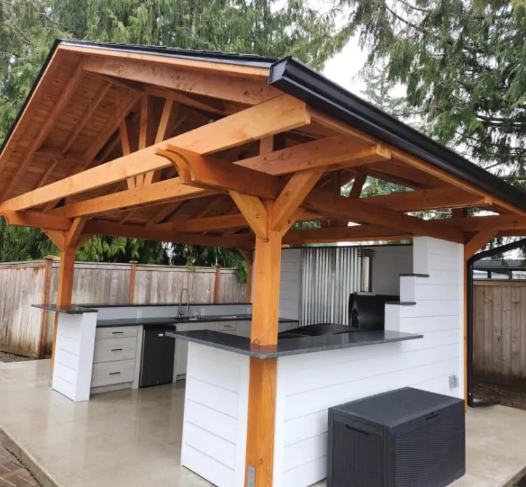 Outdoor kitchen with wooden pavilion roof, white counters, black countertops, and built-in grill.