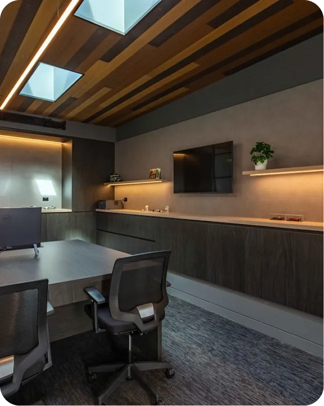 Modern office with wooden ceiling, skylights, TV on wall, dark furniture, and two mesh office chairs.