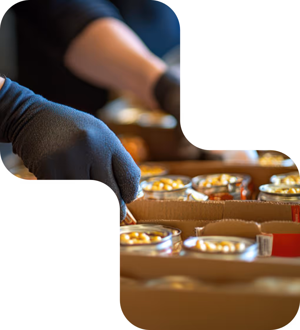 Person wearing black gloves packing canned food into cardboard boxes.