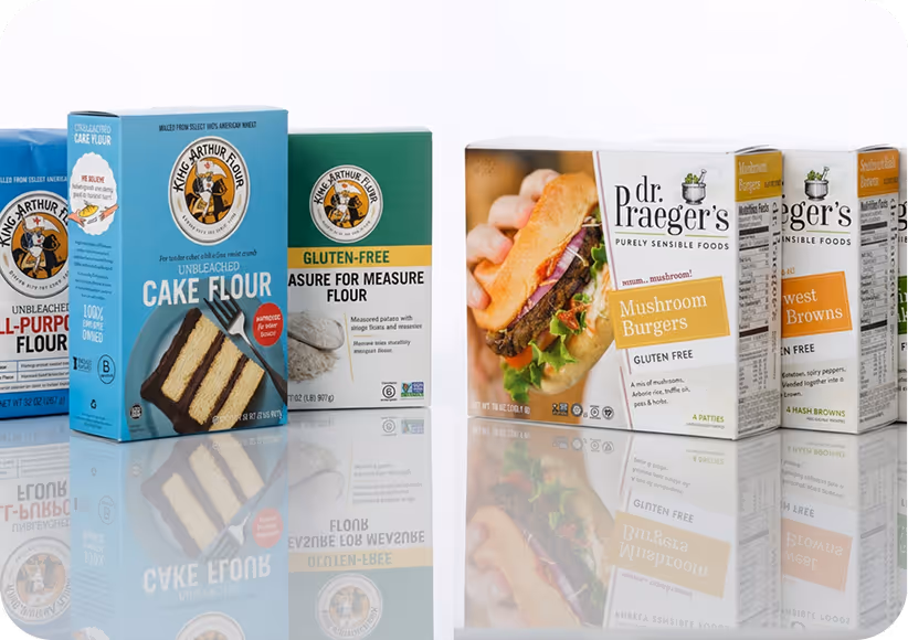 Packages of King Arthur Flour and Dr. Praeger's gluten-free food products on a reflective surface.