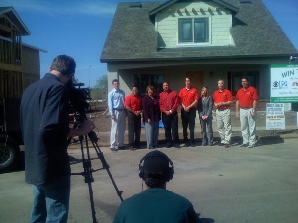A TV crew films the St. Jude Dream Home Giveaway team, many in matching red shirts, in front of the giveaway house.