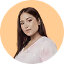Young woman with dark hair wearing a white blouse against a peach background.