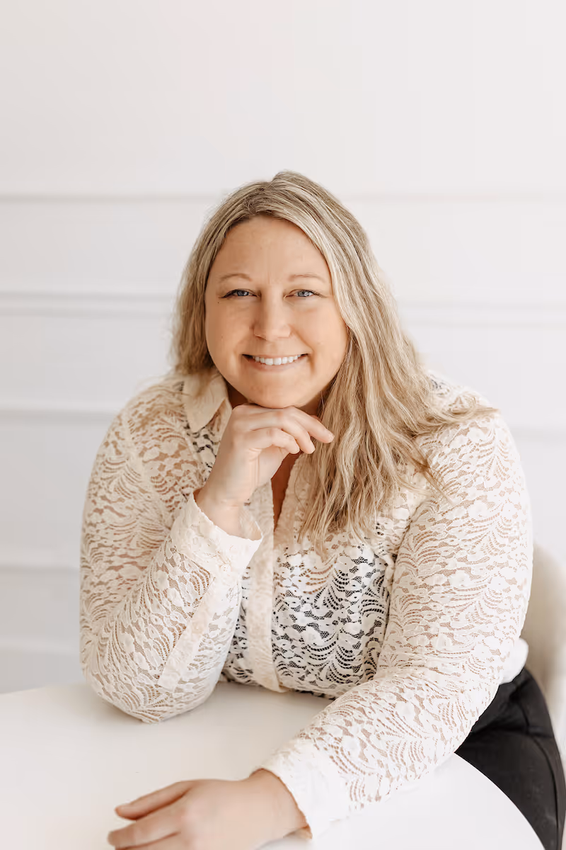 Smiling woman with straight blonde hair wearing a white shirt against a light background.