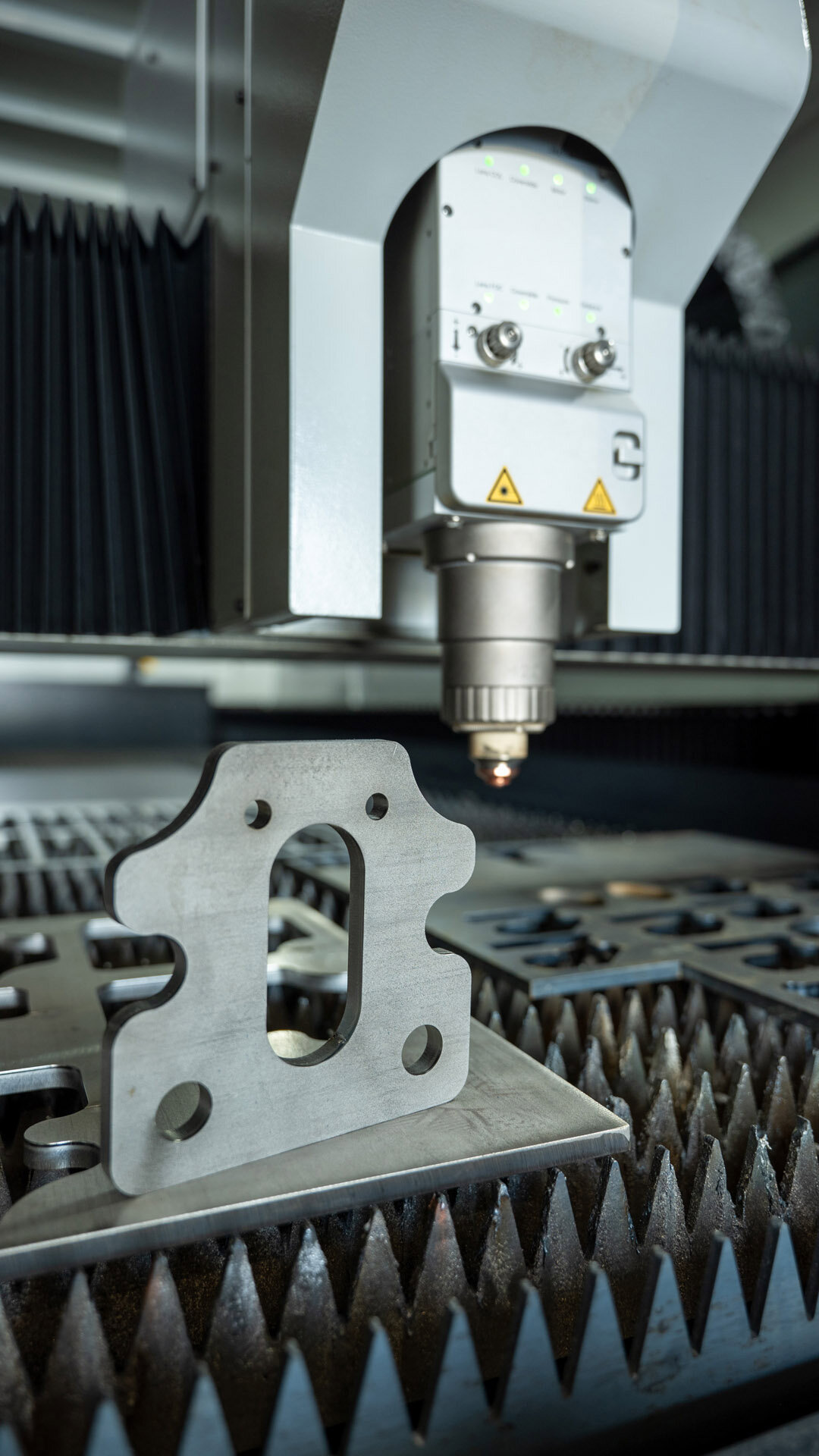 Laser cutting machine processing a flat, metal piece with multiple holes and an oval center hole.