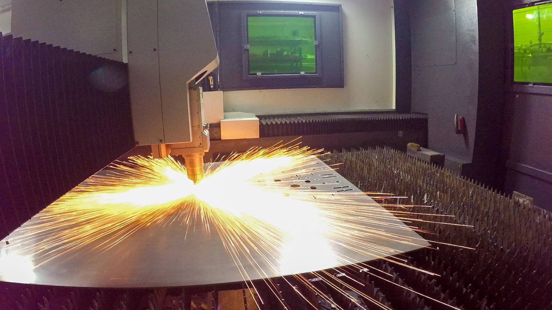 Laser cutting machine producing bright sparks while cutting a metal sheet in an industrial setting.