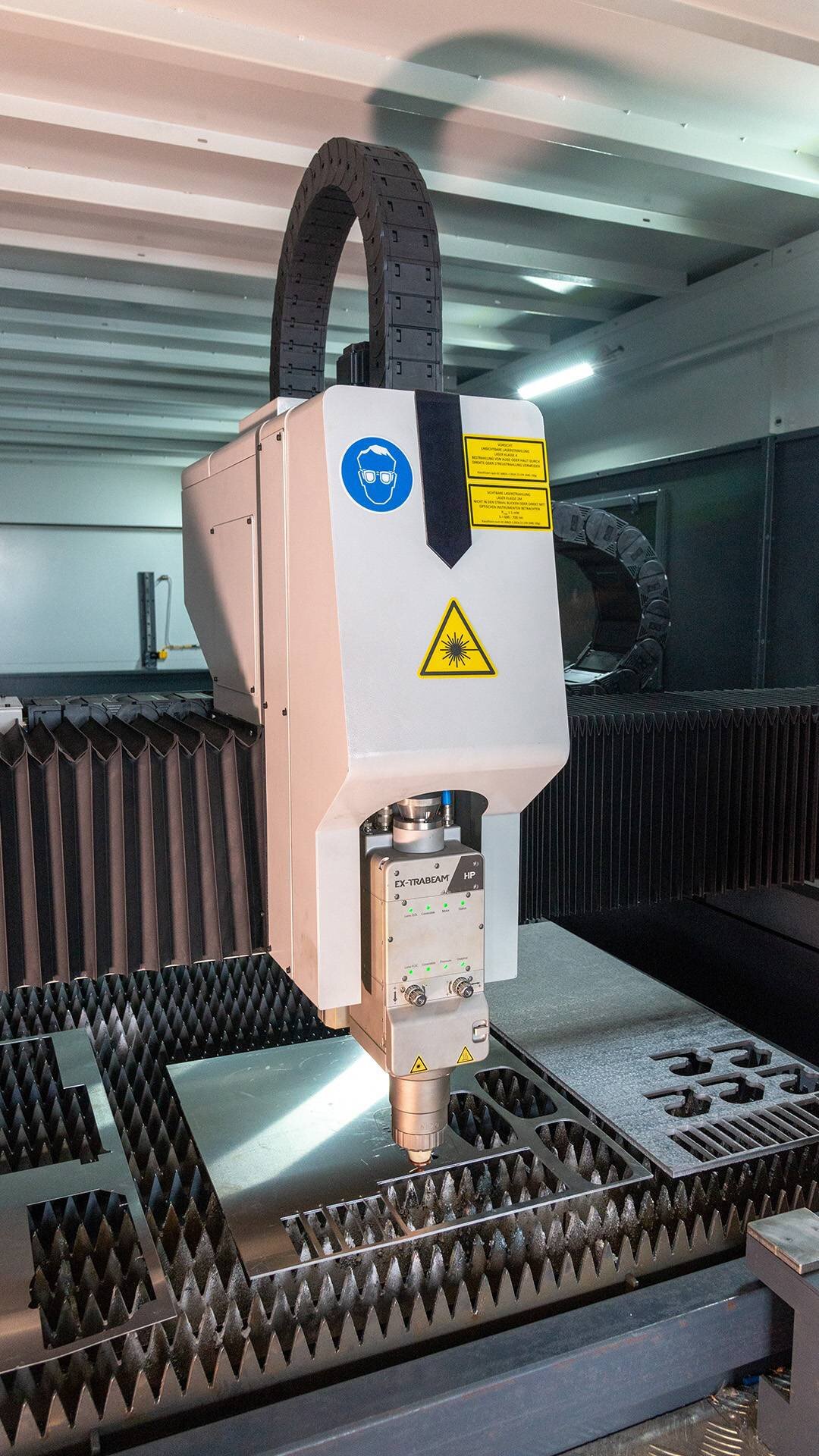 Laser cutting machine engraving metal sheet with safety and laser warning signs visible.