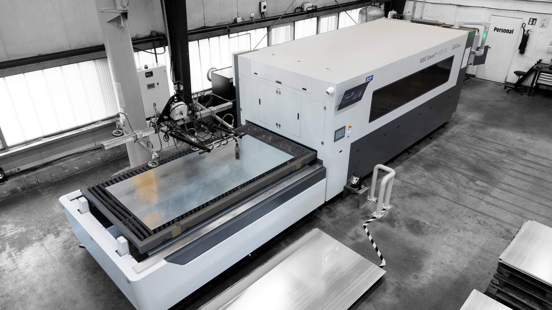 Industrial laser cutting machine handling a large metal sheet in a factory setting.