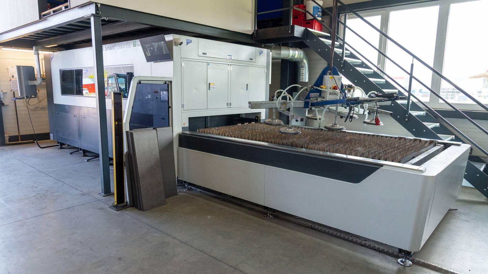 Large industrial machine with metal sheets and a suction lifting device inside a factory.