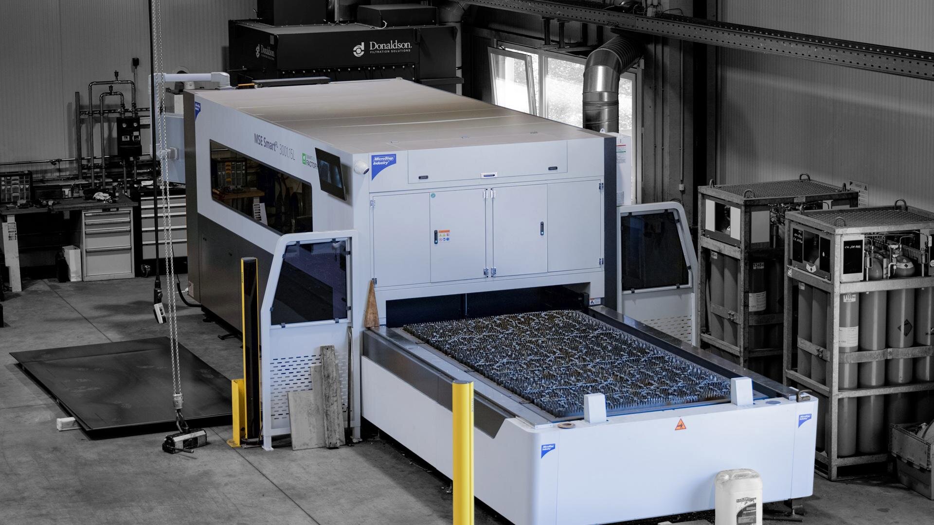 Industrial laser cutting machine in a factory with metal sheets and gas cylinders around.