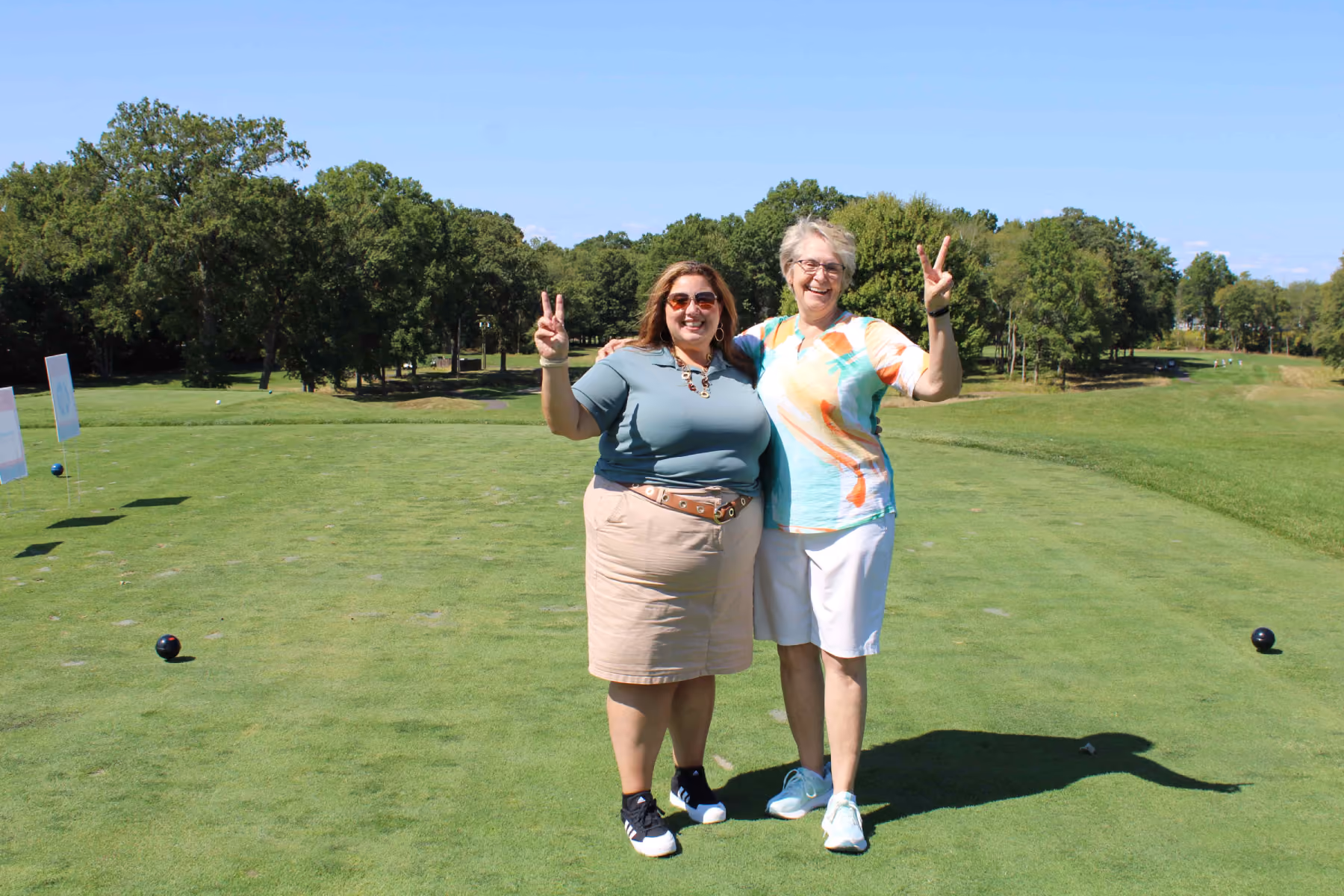 Two women smiling and posing with peace signs on a golf course at a Kelser Corporation team event
