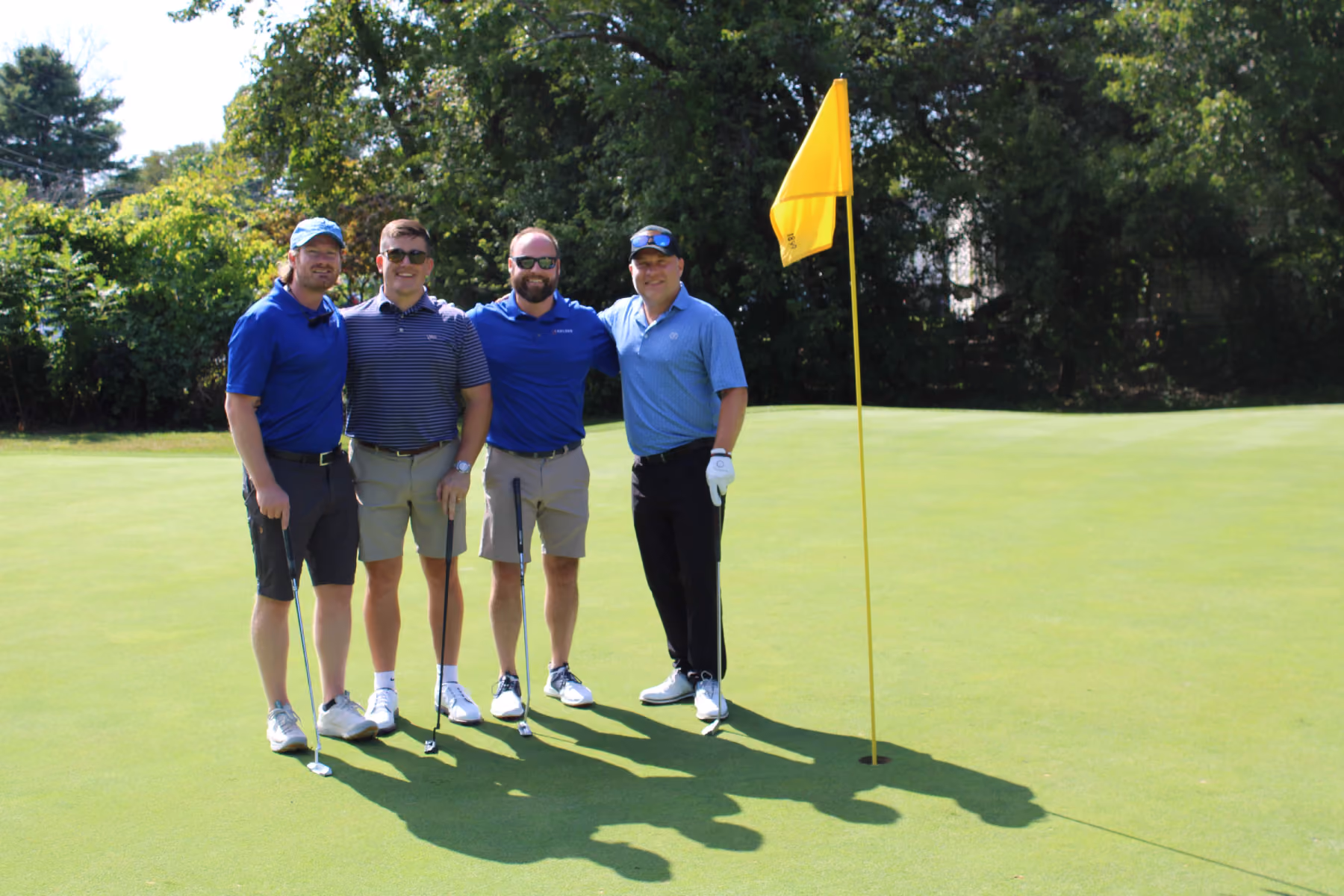 Four Kelser Corporation IT professionals posing together on a golf course green during a charity tournament event