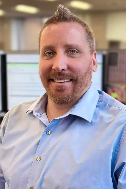 Kelser Corporation IT professional smiling in office environment with computer monitors in background