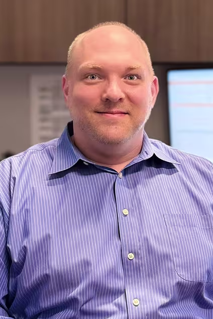 Kelser Corporation IT professional smiling at office workstation with computer monitor in background