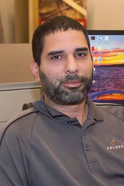 Kelser Corporation IT professional seated at office workstation with computer monitor displaying sunset desktop