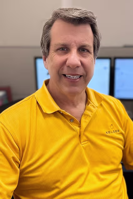 Kelser Corporation IT professional smiling in yellow branded polo shirt at workstation with monitors