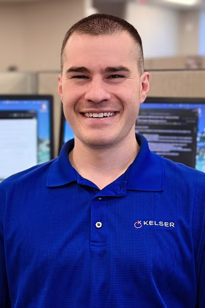 Kelser Corporation IT support technician smiling in office with computer monitors in background