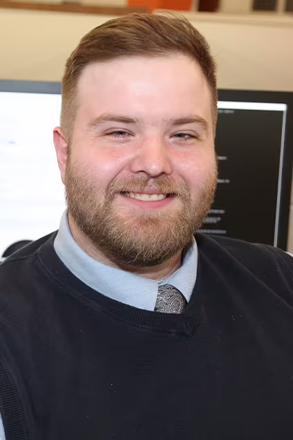 Kelser Corporation IT support team member smiling at desk with computer monitors in office