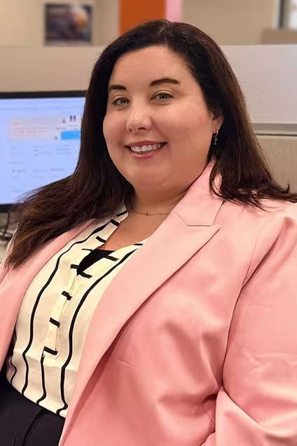 Kelser Corporation IT support specialist smiling at office workstation with computer monitor in background
