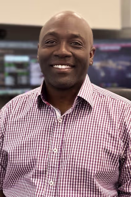 Smiling IT professional in checkered shirt seated in front of multiple monitors in a modern MSP operations center