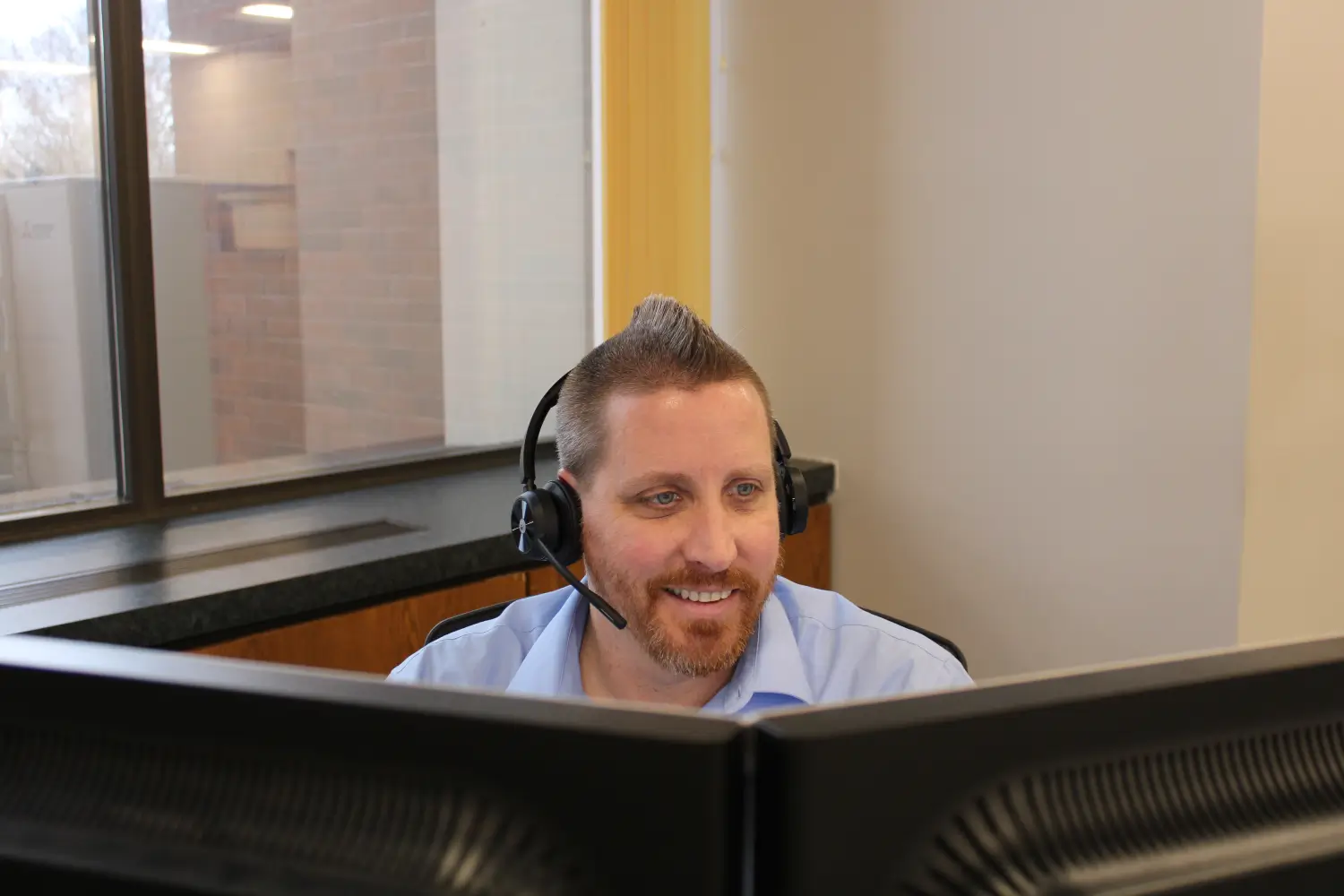 Kelser Corporation IT support specialist smiling while working at dual monitors with headset