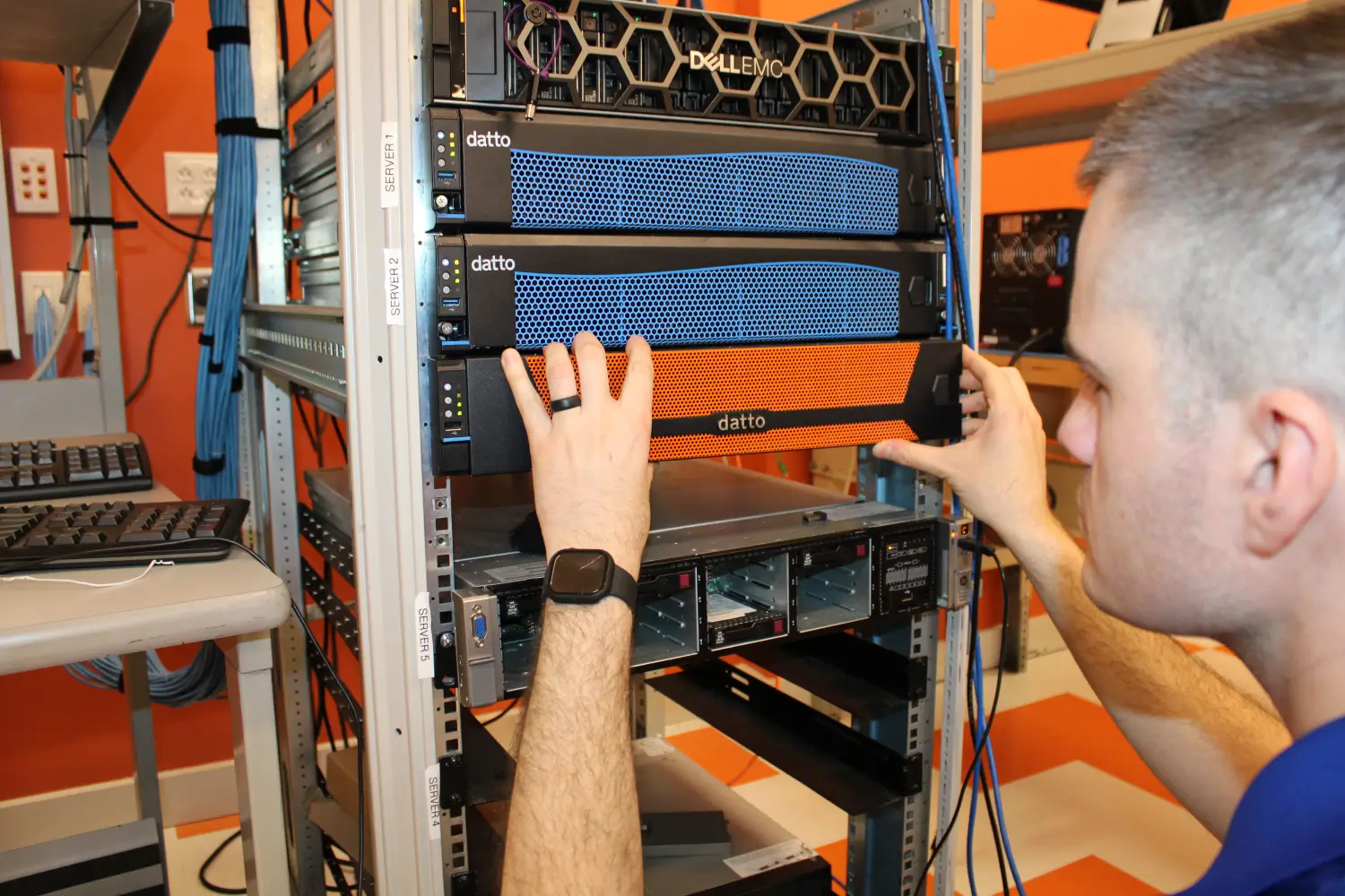IT technician installing Datto backup appliance into server rack alongside Dell EMC equipment in data center