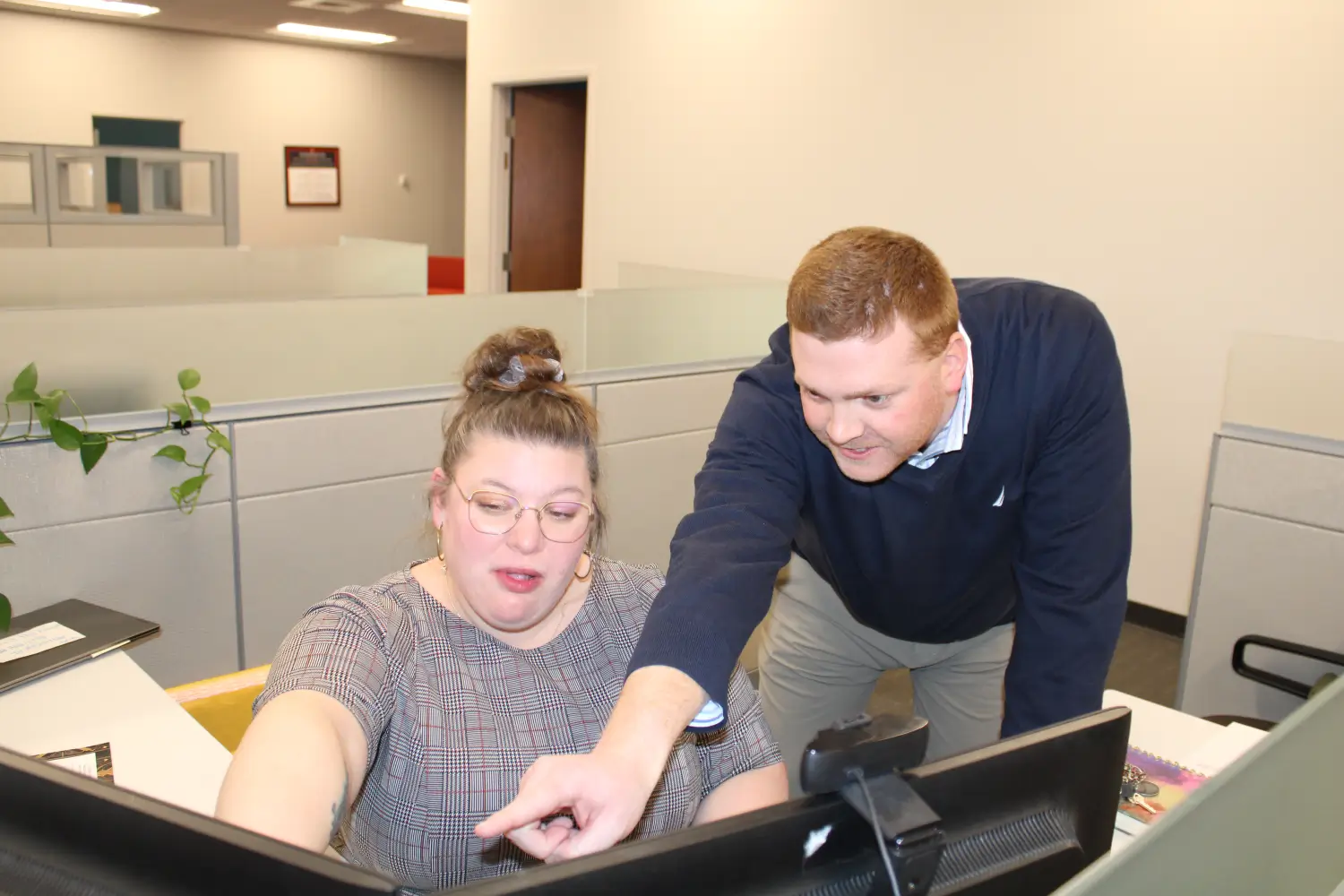 Kelser IT support technician pointing at computer screen while assisting colleague at office workstation