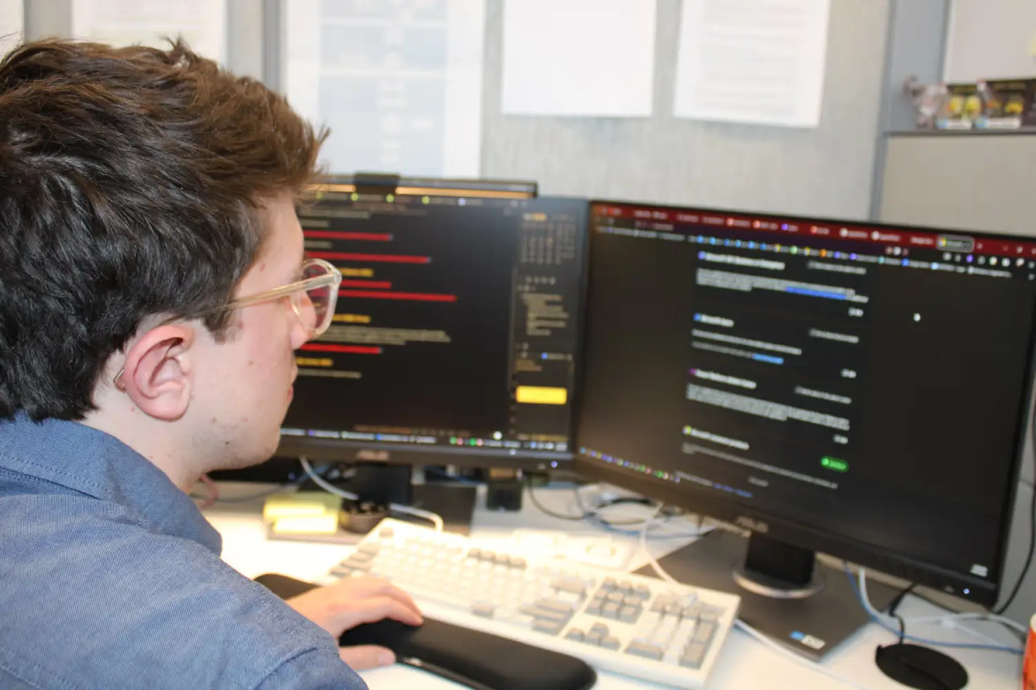 IT technician reviewing code and network management software on dual monitors at a workstation