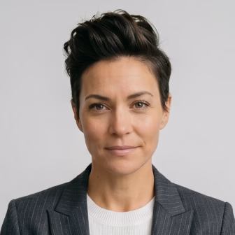 Professional headshot of a woman with dark hair wearing a gray pinstriped blazer and white ribbed shirt against a light background