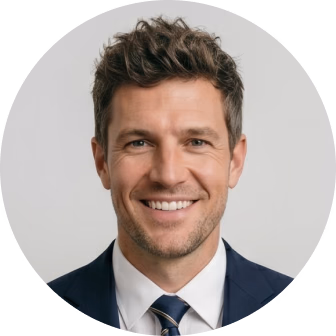 Professional headshot of a smiling man in a dark blazer and blue tie against a gray background