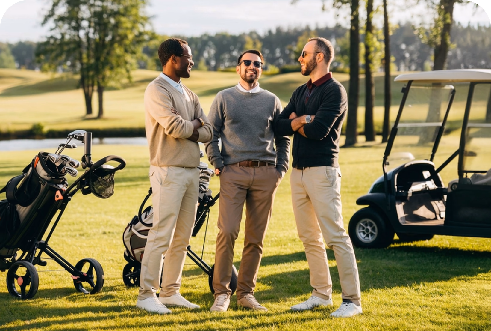 Three men in casual attire converse on a golf course with golf bags and a cart nearby