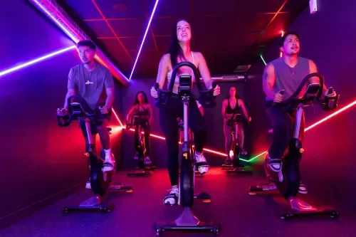 Cours collectif de vélo indoor en salle Keepcool avec participants sur vélos stationnaires sous éclairage dynamique