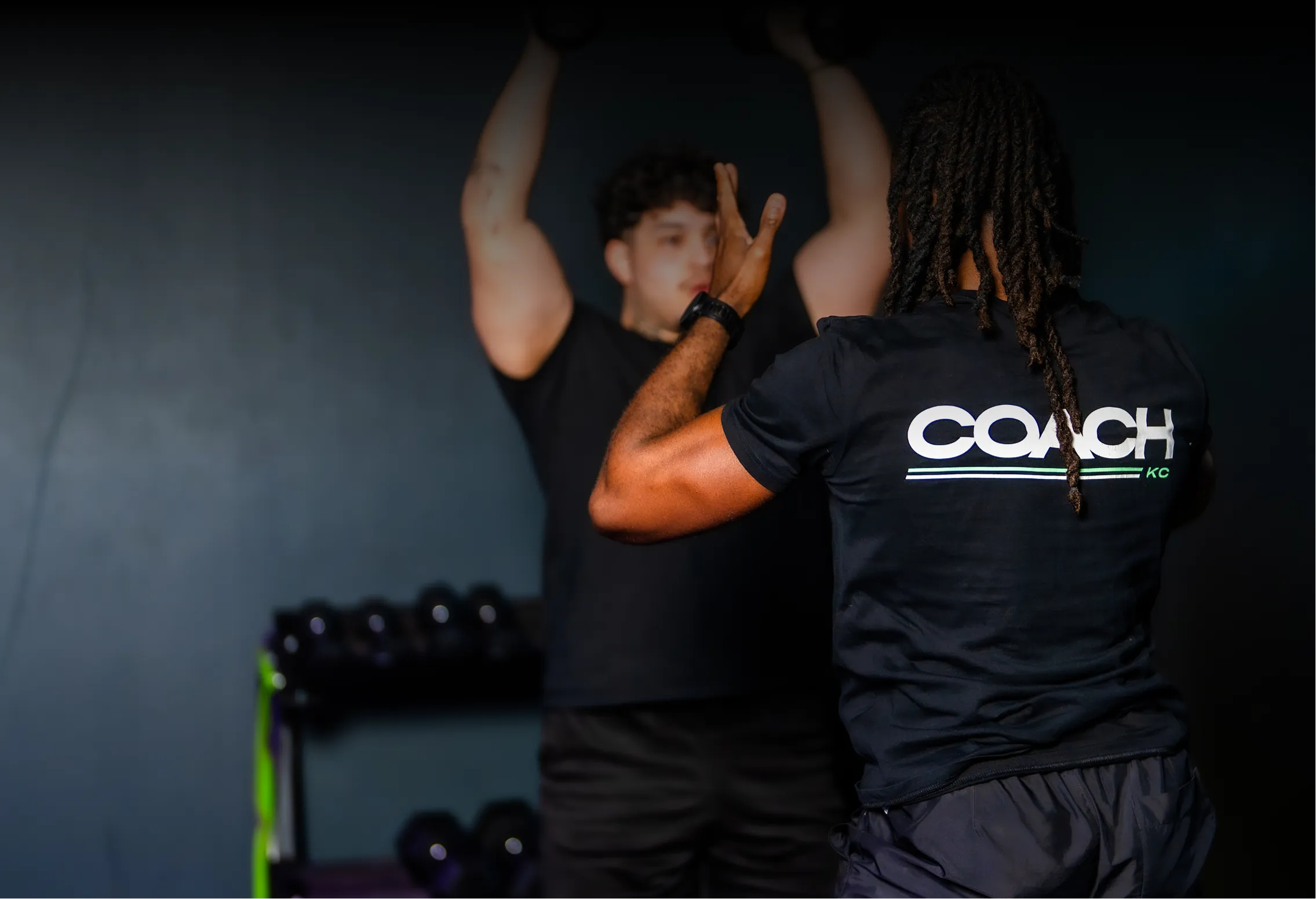 Un coach sportif guidant un homme effectuant un exercice avec les bras levés en salle de sport.