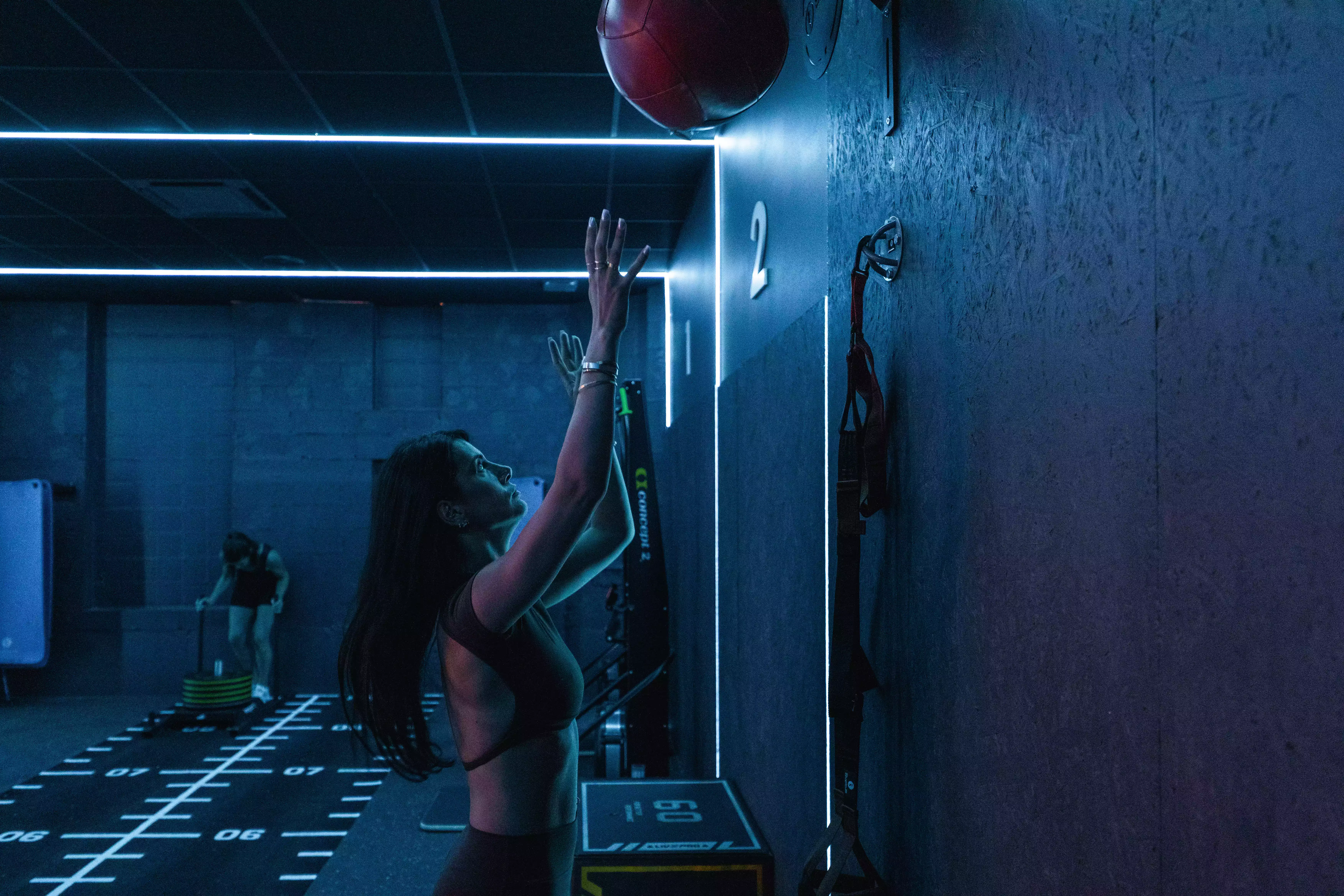 Femme en salle de sport sautant pour attraper ballon de basket, environnement lumineux et moderne.