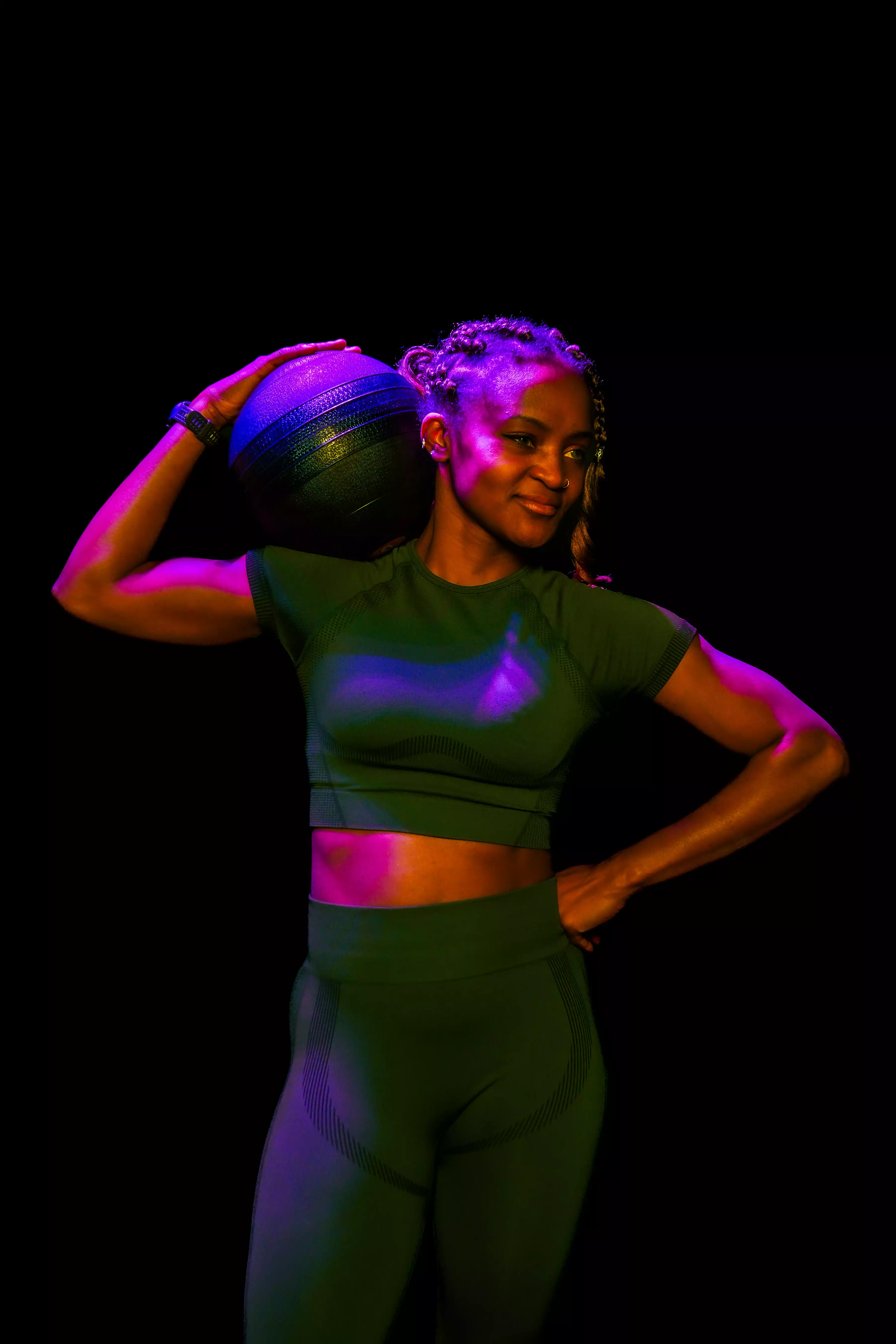 Femme en tenue sport croisée tenant boule de médicine, salle de sport ambiance lumineuse.