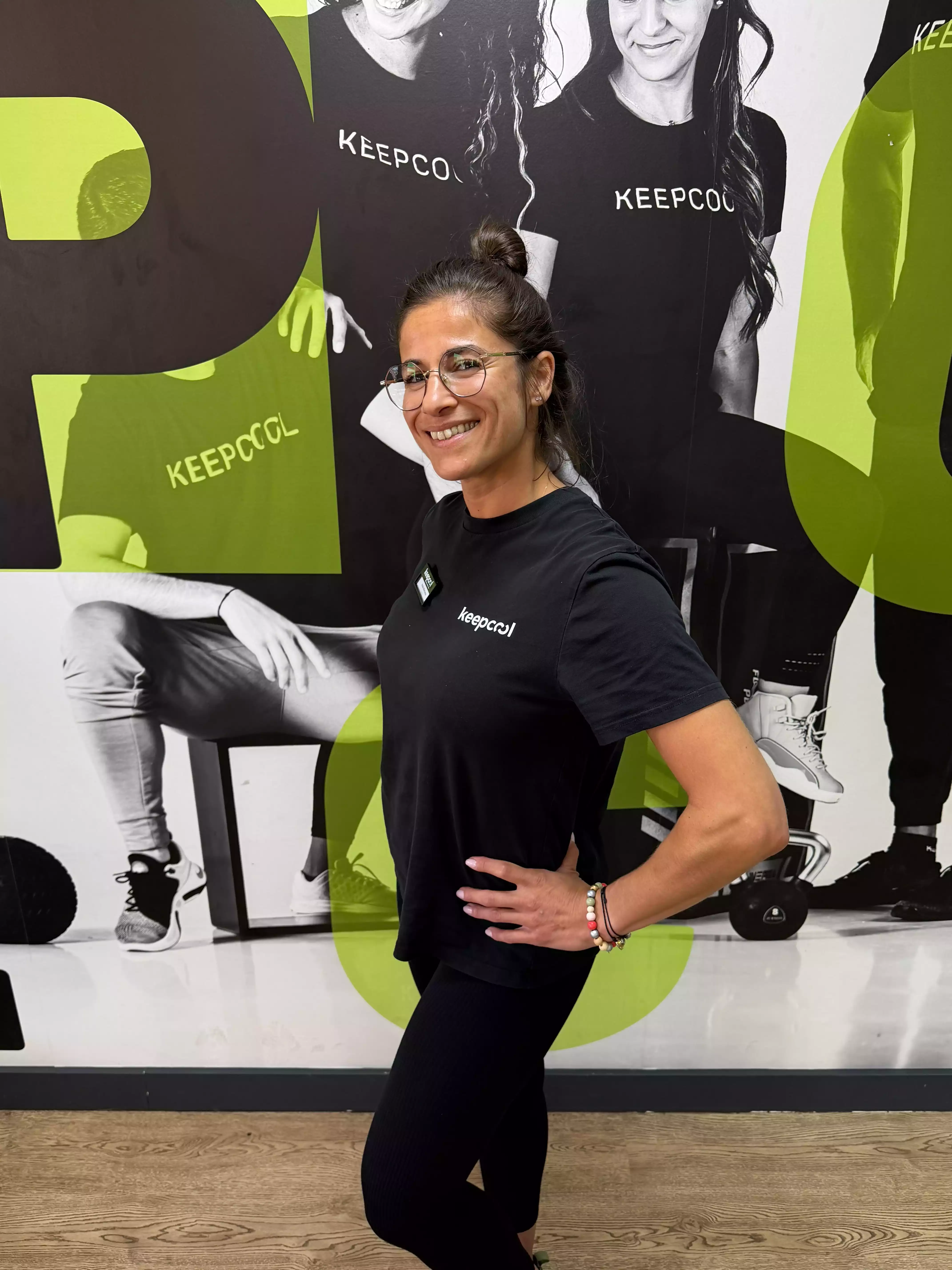 Radia, coach Keepcool, pose devant affiche promotionnelle salle sport, musculation et cours collectifs.