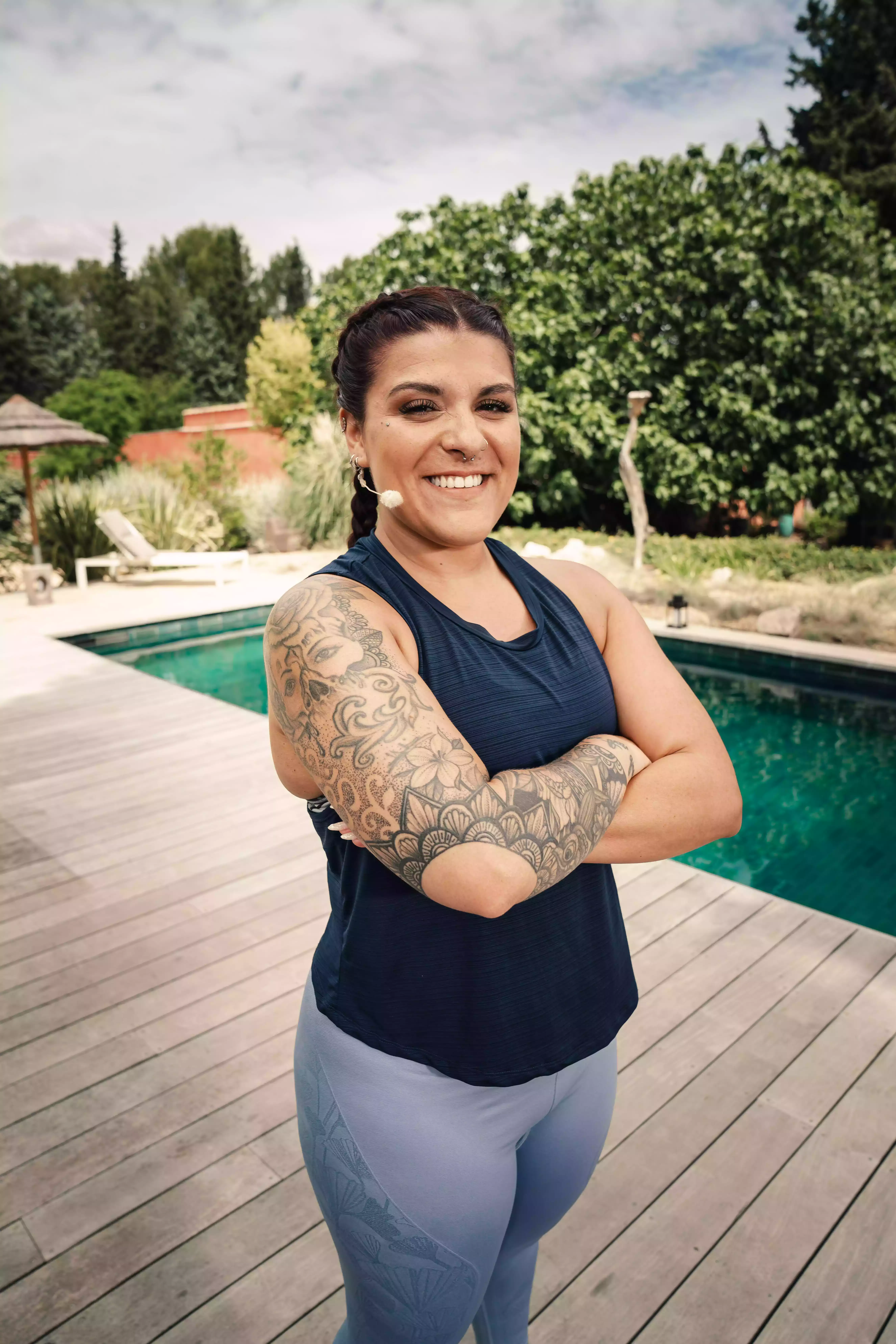 Femme souriante tatouée portant tenue sport, près piscine, ambiance salle fitness extérieur Keepcool.
