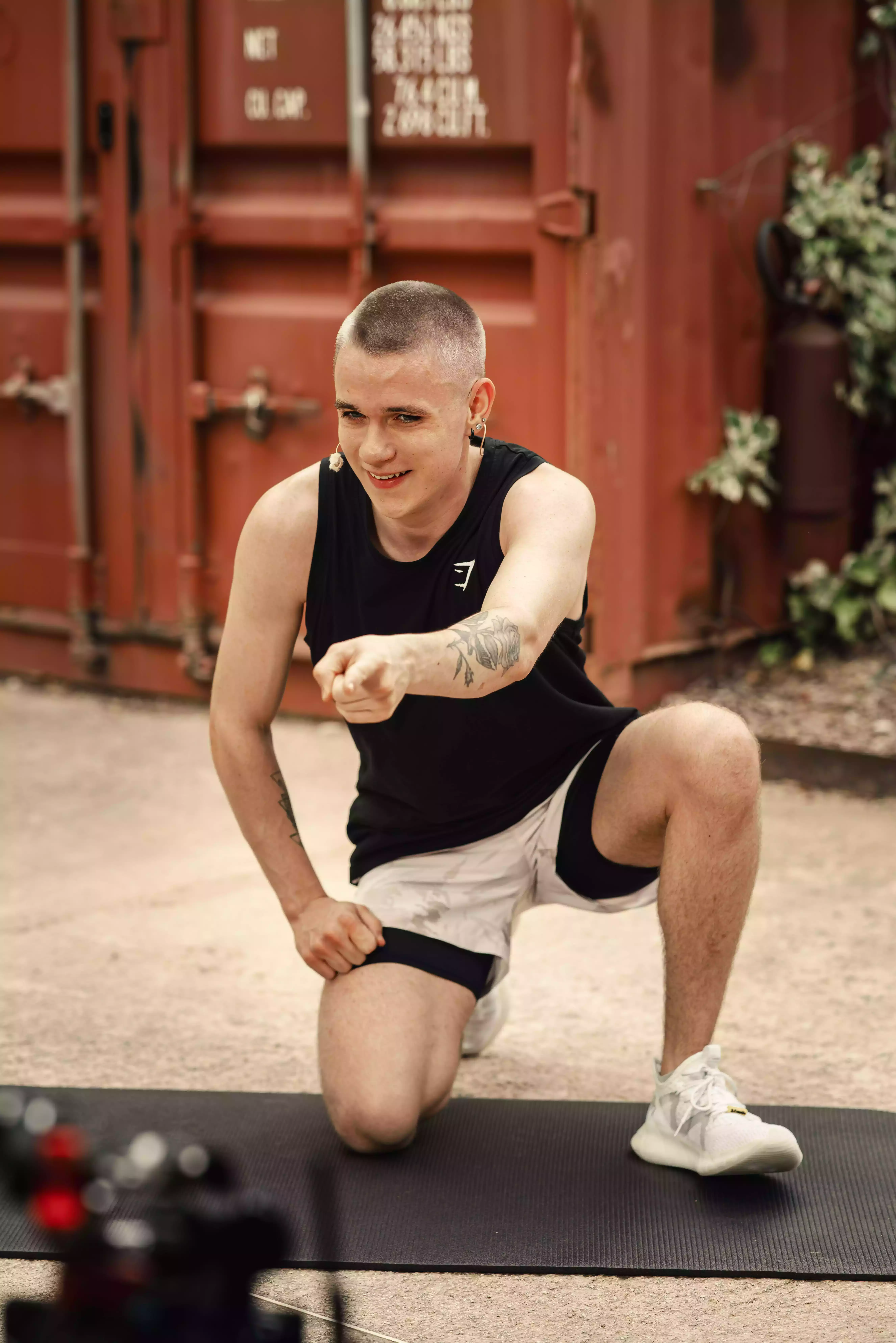 Homme en position de squat sur tapis de sport, salle fitness extérieur, entraînement musculation.