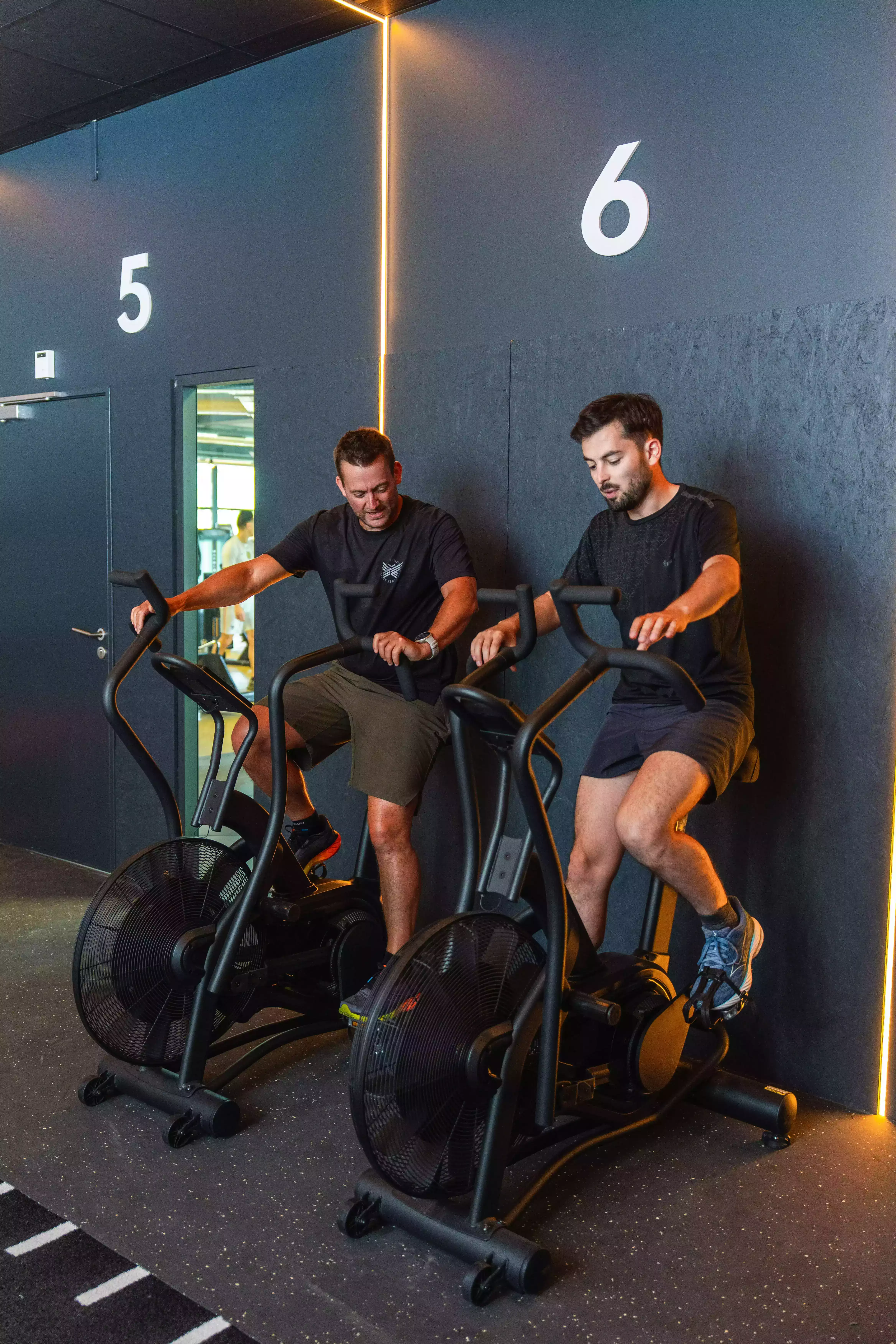 Deux hommes font du vélo d’appartement stationnaire dans une salle de sport moderne.